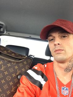 a man sitting in the back seat of a car wearing an orange shirt and hat