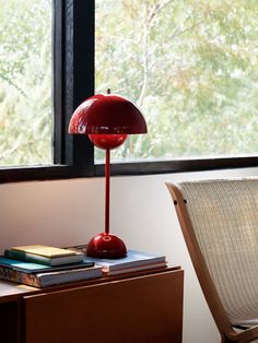 a red lamp sitting on top of a wooden table next to a chair and window