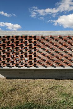 a large brick wall is shown in front of the grass and blue sky with clouds