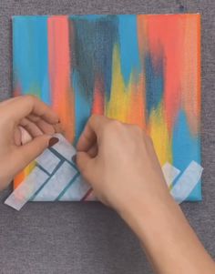 someone is painting on a piece of paper with different colors and shapes in the background