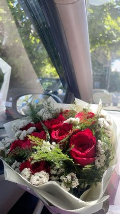 a bouquet of red roses sitting on top of a window sill in front of a car