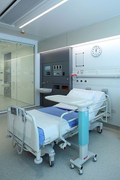 an empty hospital room with two beds and a clock on the wall