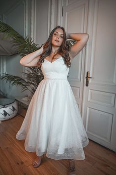 a woman in a white dress posing for the camera with her hands behind her head