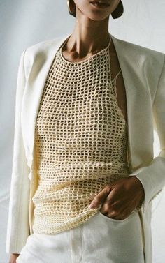 a woman wearing a crochet top and white pants with her hands in her pockets