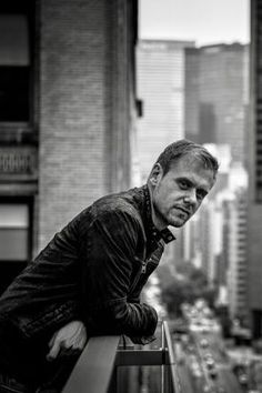 a man leaning on a ledge in front of a cityscape and looking at the camera