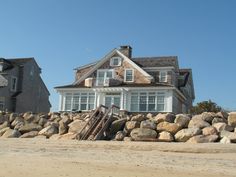 a large house sitting on top of a pile of rocks next to a sandy beach