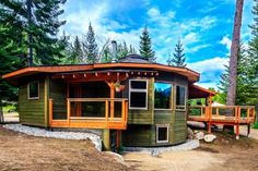 a small green house sitting on top of a dirt field next to trees and rocks