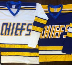 two hockey jerseys sitting on top of a wooden table next to each other in different colors