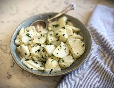 a bowl filled with potatoes on top of a table next to a blue towel and spoon