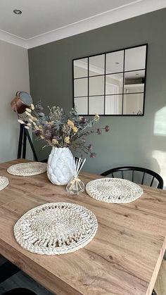 a wooden table topped with white plates and vase filled with flowers on top of it