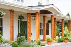 the front porch of a white house with green doors and flowers in pots on either side