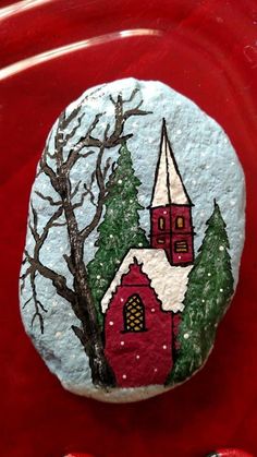 a painted rock with a church and trees on it in front of a red background