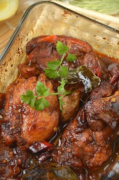 a glass dish filled with meat covered in sauce and garnished with cilantro