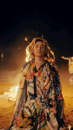 a man sitting on top of a sandy beach next to a fire pit at night