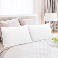 a bed with white sheets and pillows on top of it next to a table with flowers