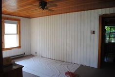 an empty room with a ceiling fan and wooden paneling on the wall behind it