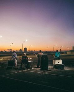 four people are sitting on suitcases in an airport tarmac at sunset or dawn