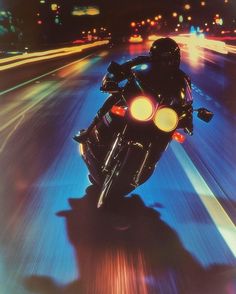 a person riding a motorcycle on a city street at night with bright lights in the background