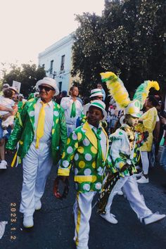 two men in green and yellow costumes walking down the street with other people behind them