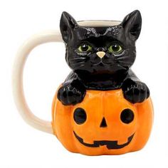 a black cat sitting on top of a halloween pumpkin coffee mug with its eyes open