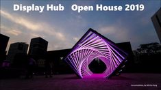 an abstract sculpture is lit up with purple light in the middle of a city square