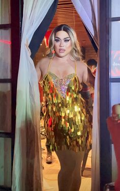 a woman in a gold and green costume is standing by a window with her hands on her hips