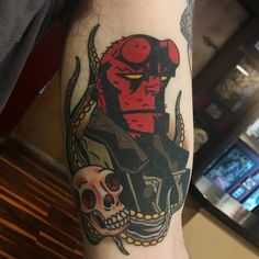 a man with a tattoo on his arm has a red devil and two skulls in front of him