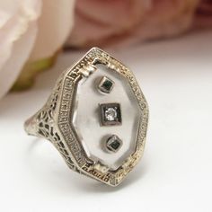 This Beautiful Art Deco Came Out Of A Well-Known Antique Jewelry Dealer's Private Collection. Finely Detailed Vintage Art Deco Rock Crystal, Diamond And Emerald Ring (Circa 1920s To 1930s) Crafted In 10k White Gold With A Filigree Setting. The Fanciful Ring Has A Small Center Diamond With Two Flanking Emeralds Set In Frosted Rock Crystal. The Face Of The Ring Measures Approx. 13.50 Mm By 8.96 Mm. Ring Is A Us Size 5.5 And Is Sizeable. It Weighs 2.88 Grams And Is In Excellent Condition. A Really Special Old Ring! Our Rings Come Ready For Gift-Giving With Velvet Presentation Boxes. Box In Photos For Display Purposes. White Platinum Ring With Accent Stones, Vintage White Rings With Accent Stones, Antique White Filigree Ring With Diamond Cut, Antique White Filigree Ring For Formal Occasions, White Filigree Fine Jewelry, White Fine Jewelry With Filigree Details, White 14k Gold Jewelry With Single Cut Diamonds, Heirloom White Diamond Cut Jewelry, White Fine Jewelry With Filigree