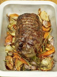 a large piece of meat sitting in a white container filled with carrots, onions and other vegetables