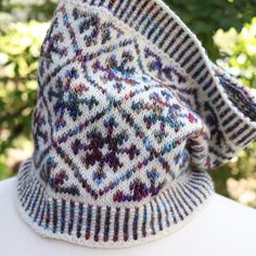 a knitted hat sitting on top of a white table next to some trees and bushes