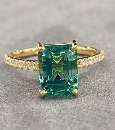 an emerald and diamond ring sitting on top of a gray surface with diamonds around it