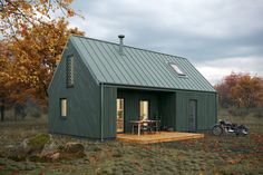 a small green house with a motorcycle parked in front of it and autumn leaves on the ground