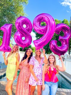 three women holding up large pink balloons in front of a fountain with the number twenty nine on it