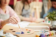 people sitting at a table with paint and brushes in front of them, while one woman is painting