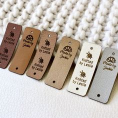 six leather tags with the names of different types of items on them, lined up against a white blanket