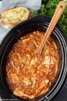 a crock pot filled with chicken and tomato soup next to bread on a table