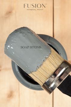 the brush is being used to paint a wooden wall with grey paint on it and says, soap stone