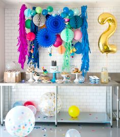 a table with balloons, streamers and confetti on it in front of a white brick wall