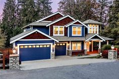 a large blue house with two garages in the front yard and trees behind it