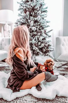 a woman sitting on the floor next to a christmas tree with a dog in her lap