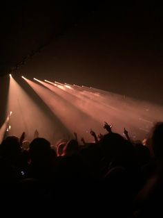 the crowd is at a concert with their hands in the air and lights shining down on them