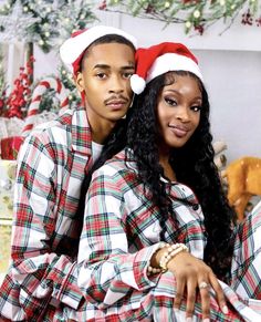 a man and woman sitting next to each other in front of a christmas tree wearing santa hats