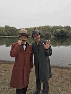 two men standing next to each other in front of a lake