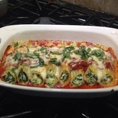 a casserole dish with spinach, cheese and sauce in it on the stove