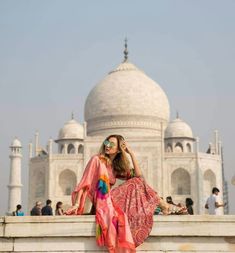 a woman sitting on the edge of a wall in front of a white marble building