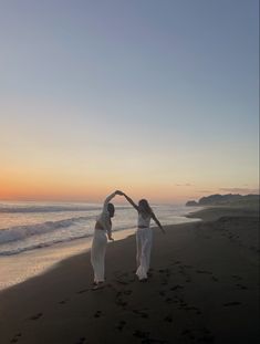 two women are dancing on the beach at sunset