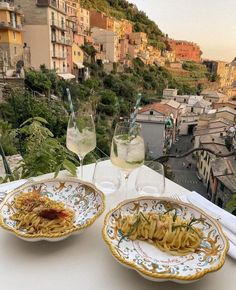 two plates with pasta and wine on a table in front of a cityscape