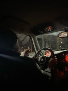 a man driving a car in the dark with his hand on the steering wheel while another person sits behind him