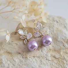 Beautiful Bridesmaid earrings feature an elegant Lavender Glassl pearl drop accompanied by dazzling cz crystals encrusted in gold plating. Simple and visually stunning, this design is the perfect accessory for a modern bride. The Details: * Made with premium quality crystals and lavender glass pearls * Stones are hand set in secure prongs * Great for brides, bridesmaids, mother of the bride, mother of the groom * Great for weddings, engagements, proms, and other special events Perfect earrings f Purple Teardrop Earrings For Wedding, Elegant Purple Wedding Earrings, Purple Dangle Bridal Earrings For Wedding, Purple Drop Earrings For Wedding, Gold Bridesmaid Earrings, Lilac Earrings, Lavender Earrings, Bridesmaid Earrings Gold, Pearl Earrings Wedding