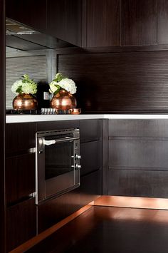 two vases with flowers sit on the counter top in this modern, dark kitchen